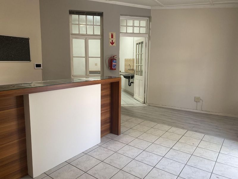 An office reception area featuring a built-in counter, mixed flooring, and access to a secondary utility space with a sink.