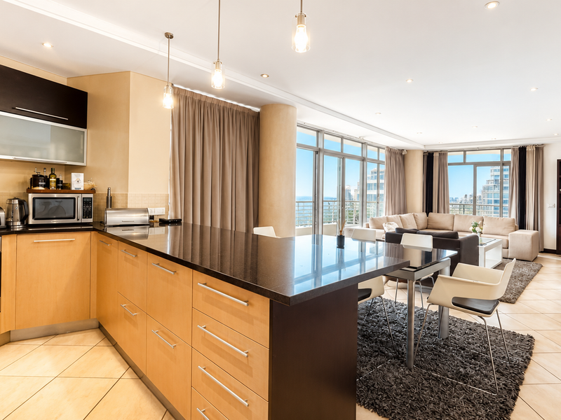 Spacious open-plan living area featuring a modern kitchen with granite countertops, integrated appliances, and large sliding doors leading to a balcony with city views.