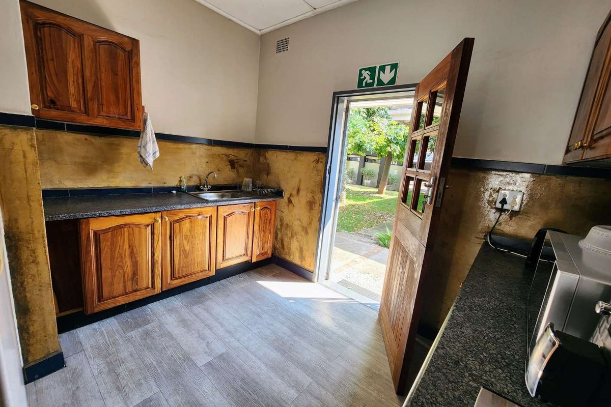 A functional kitchen area featuring wooden cabinetry, granite-look countertops, a stainless steel sink, and direct access to the rear garden.