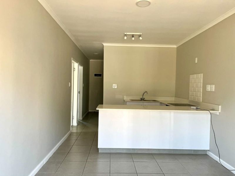 An open-plan living and kitchen area featuring tiled flooring, a breakfast counter, and a neutral color palette, offering a clean and functional space.