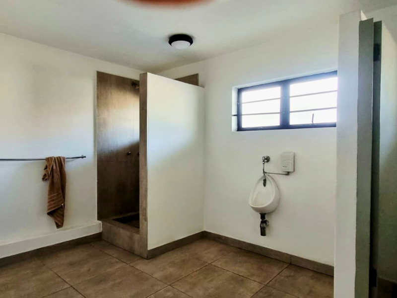Functional industrial-style bathroom featuring a tiled shower enclosure, wall-mounted urinal, and security-barred window, providing basic utility and clean finishes.