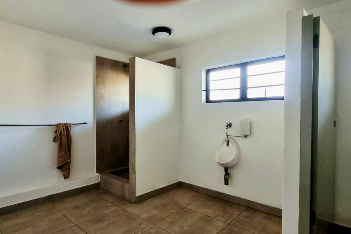 Functional industrial-style bathroom featuring a tiled shower enclosure, wall-mounted urinal, and security-barred window, providing basic utility and clean finishes.