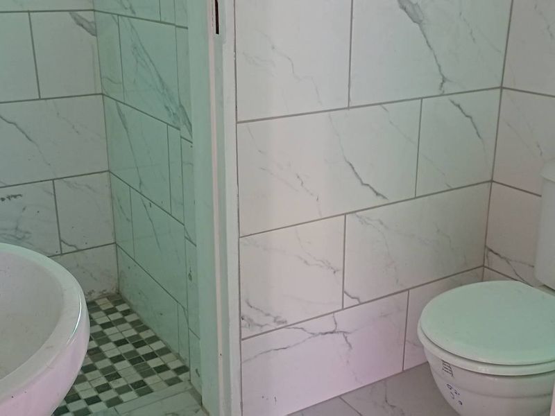 A clean, modern bathroom featuring marble-look wall tiles, a pedestal basin, a toilet, and a separate shower enclosure.