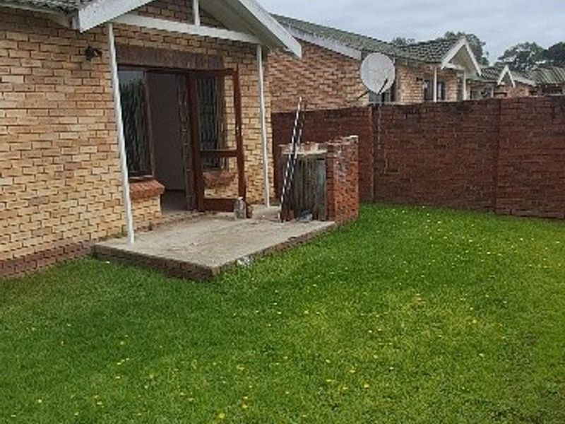 Rear view of the townhouse featuring a private garden, brick boundary wall, and a small concrete patio area.