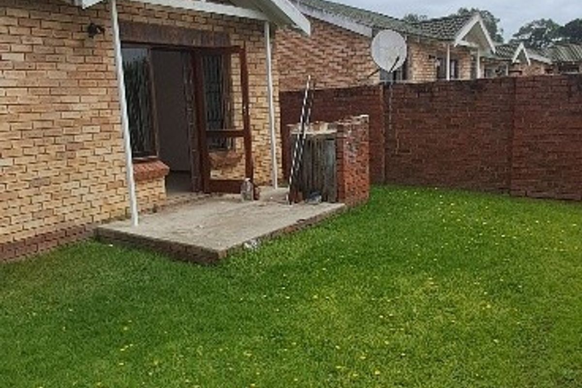 Rear view of the townhouse featuring a private garden, brick boundary wall, and a small concrete patio area.