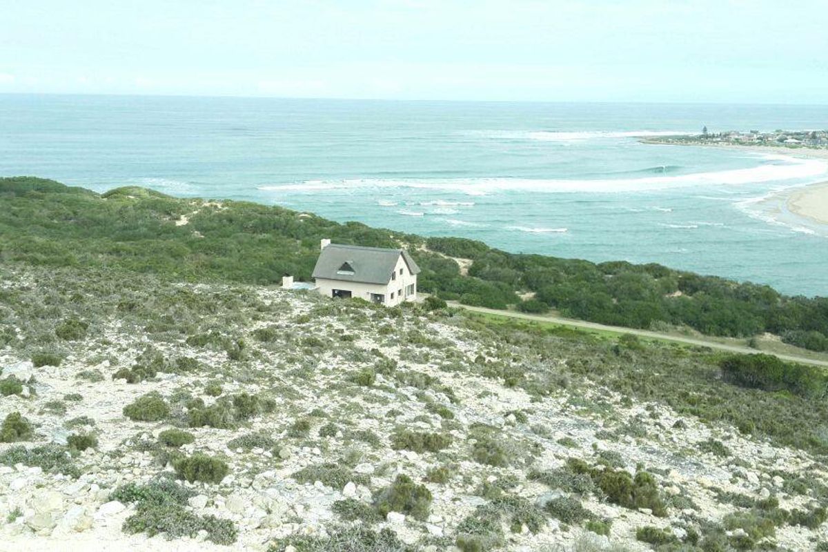 An elevated aerial view showcasing the property's coastal location, featuring a detached house situated on a hillside overlooking the ocean and beach.