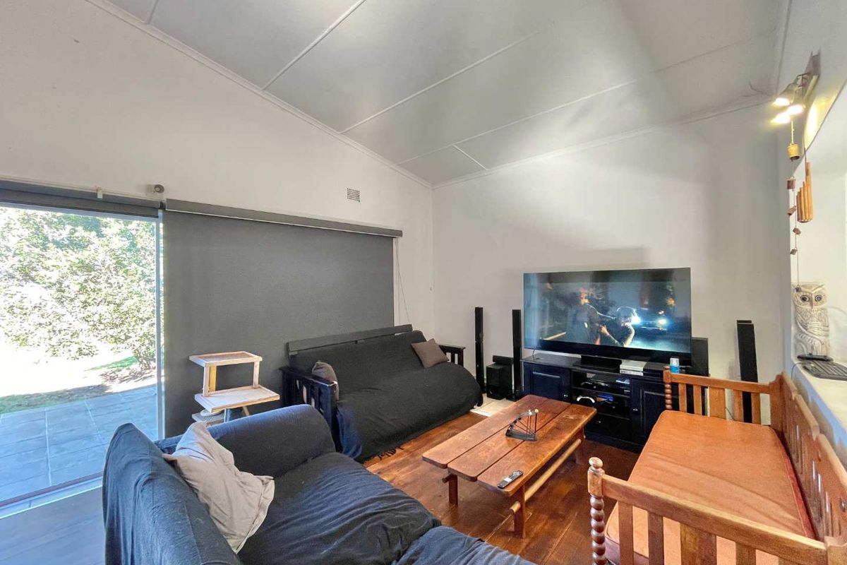 A spacious living room featuring vaulted ceilings, timber flooring, and large sliding glass doors providing direct access to the outdoor patio area.