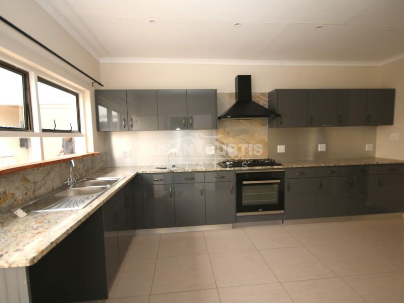 Modern kitchen featuring dark grey cabinetry, granite countertops, built-in oven, gas hob, and extractor fan with tiled flooring.