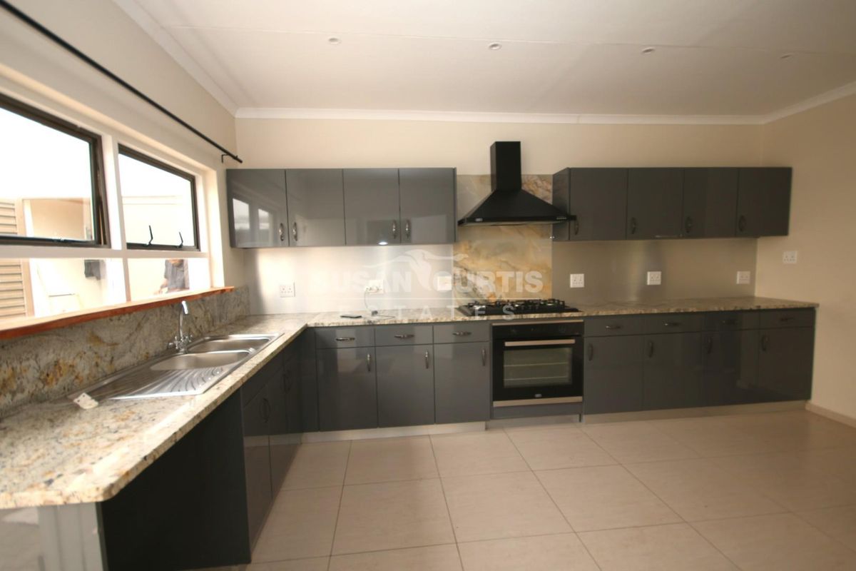 Modern kitchen featuring dark grey cabinetry, granite countertops, built-in oven, gas hob, and extractor fan with tiled flooring.