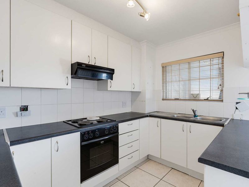 A functional kitchen featuring white cabinetry, dark laminate countertops, an integrated electric stove and oven, and a double sink with tiled backsplash.