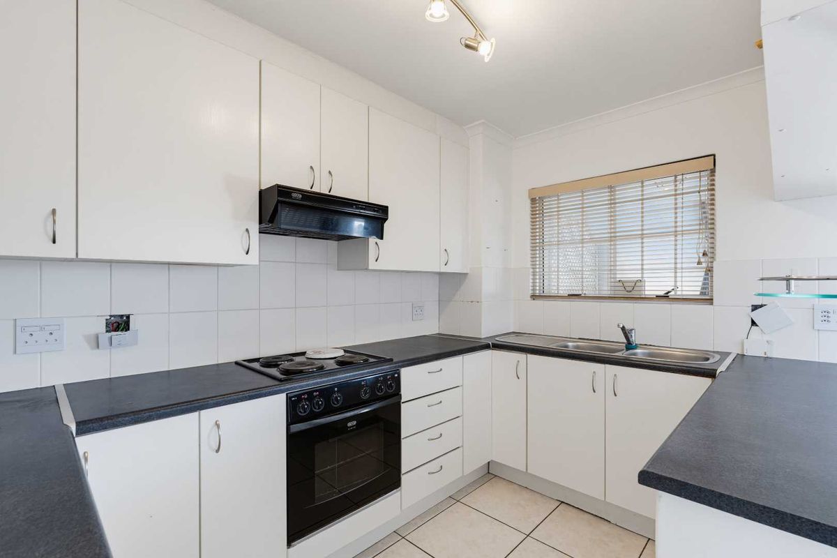 A functional kitchen featuring white cabinetry, dark laminate countertops, an integrated electric stove and oven, and a double sink with tiled backsplash.