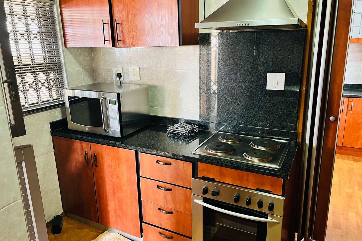 A compact kitchen featuring wood-finish cabinetry, granite countertops, a built-in electric hob, oven, and stainless steel extractor fan.