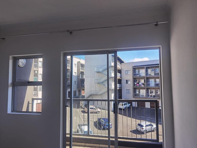 An empty living area featuring a sliding glass door that opens onto a balcony with views of the apartment complex parking area.