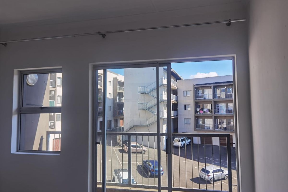An empty living area featuring a sliding glass door that opens onto a balcony with views of the apartment complex parking area.