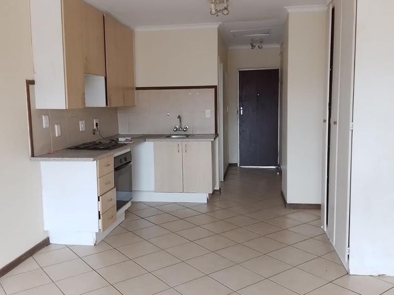 A functional kitchen area featuring built-in cabinetry, a hob, an oven, and tiled flooring, leading into an open-plan living space.