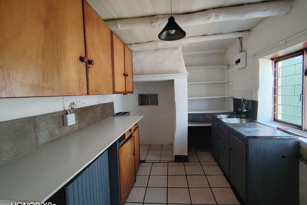 A dated kitchen featuring wooden cabinetry, tiled flooring, and exposed beam ceilings, offering a functional layout ready for modernization and renovation.