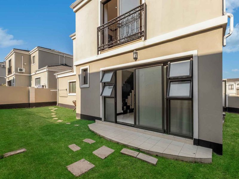 Rear view of the property featuring a tiled patio, sliding glass doors, and a small balcony with wrought iron railing overlooking the garden.