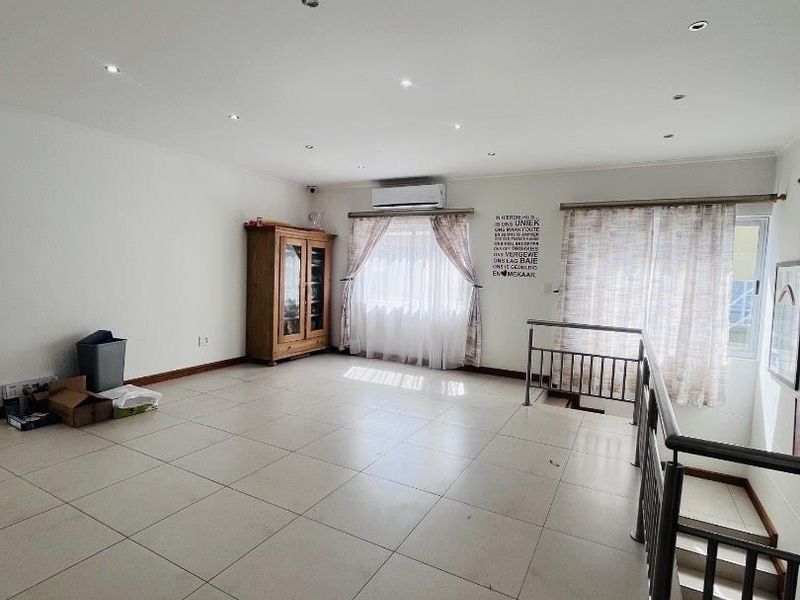 Spacious open-plan living area featuring large format floor tiles, recessed lighting, and a split-system air conditioner, with an adjacent staircase.