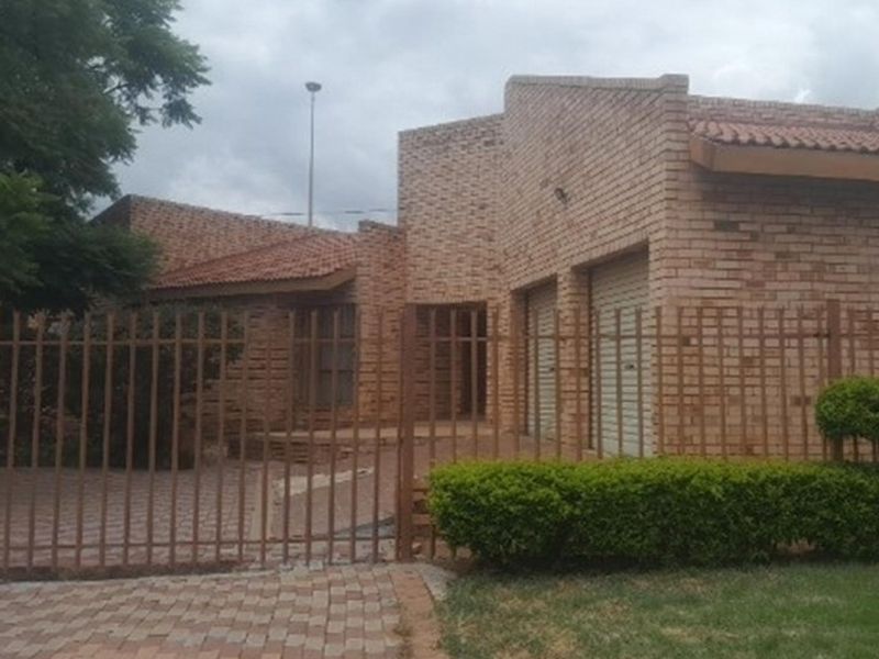 Front elevation of a face brick house featuring a double garage, paved driveway, and secure metal perimeter fencing.
