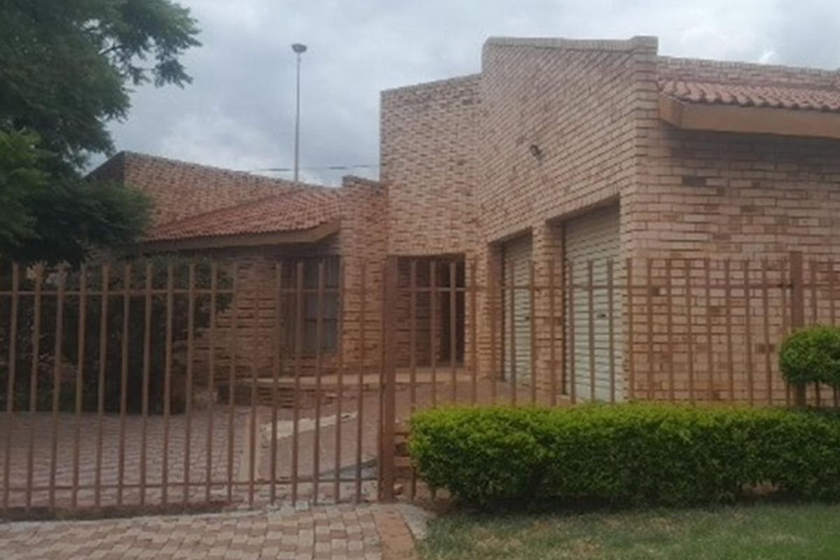 Front elevation of a face brick house featuring a double garage, paved driveway, and secure metal perimeter fencing.