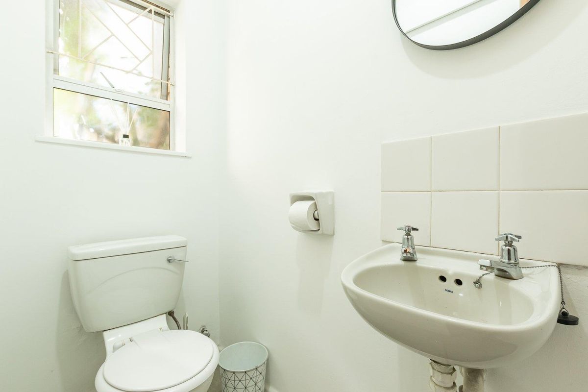 A compact guest bathroom featuring a white ceramic toilet, wall-mounted basin with chrome taps, and a window with security bars.
