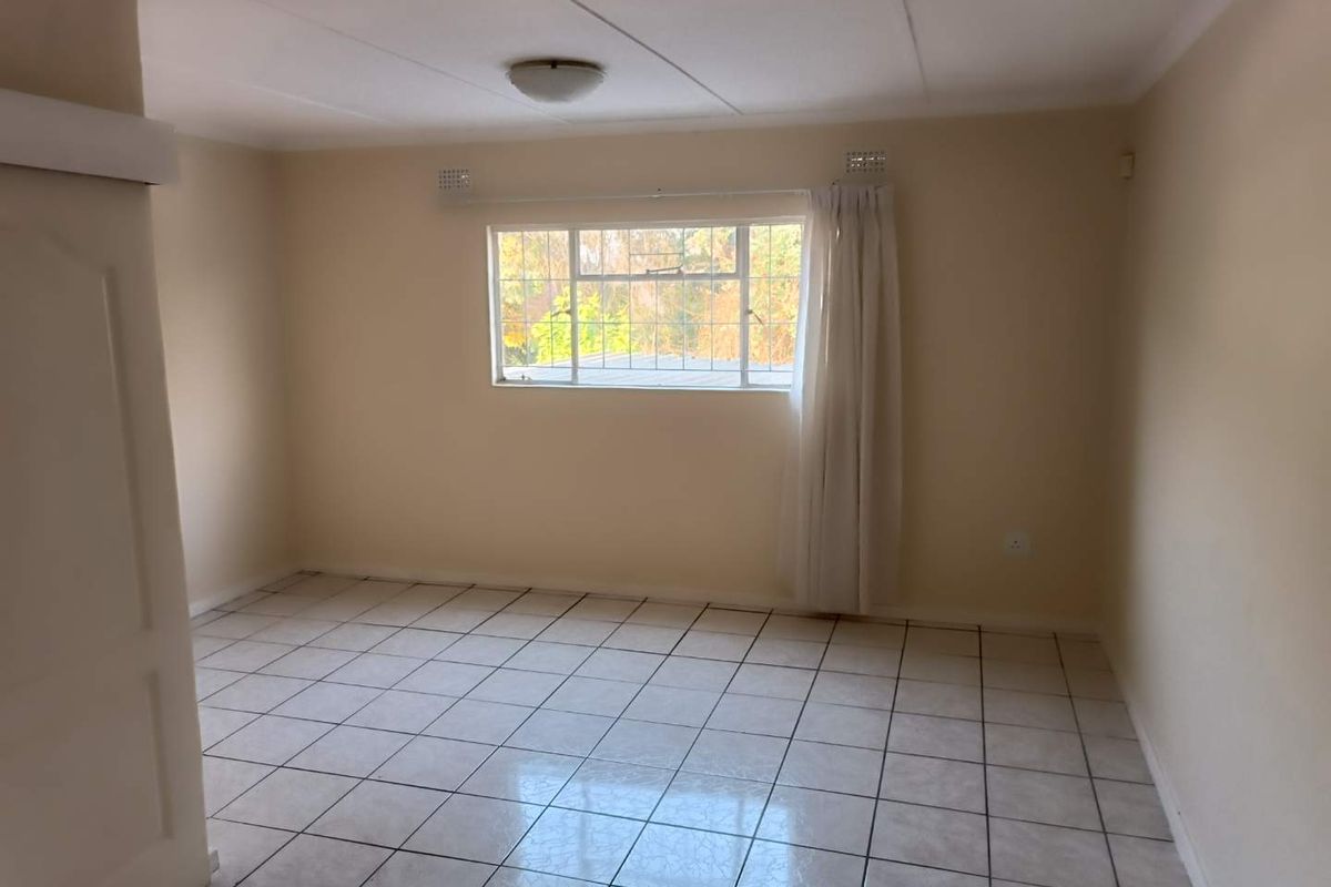 A vacant bedroom featuring neutral walls, tiled flooring, and a window with security bars, offering a blank canvas for personalization.