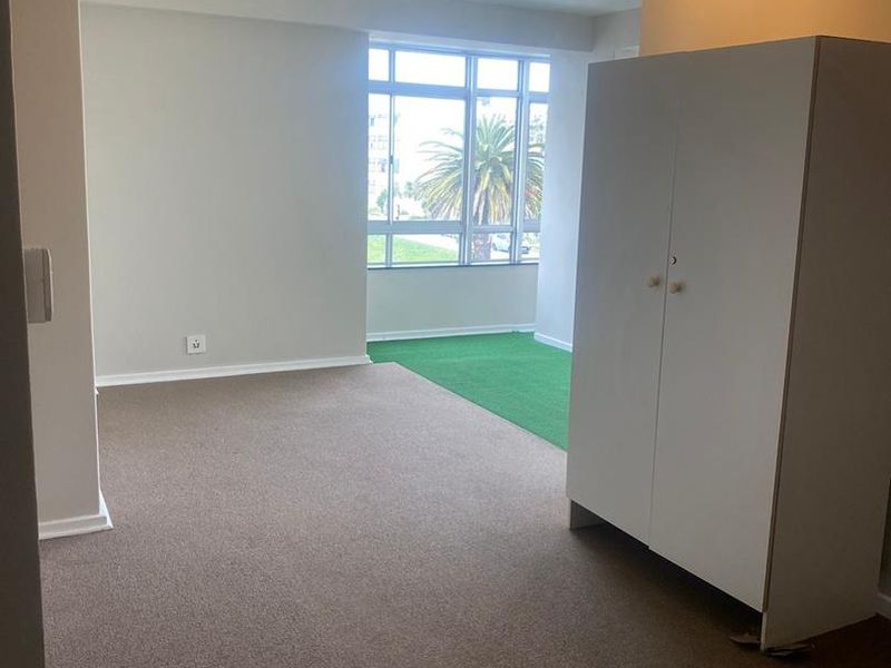 A spacious, carpeted living area featuring a large window that allows for natural light, providing a neutral canvas for interior design.