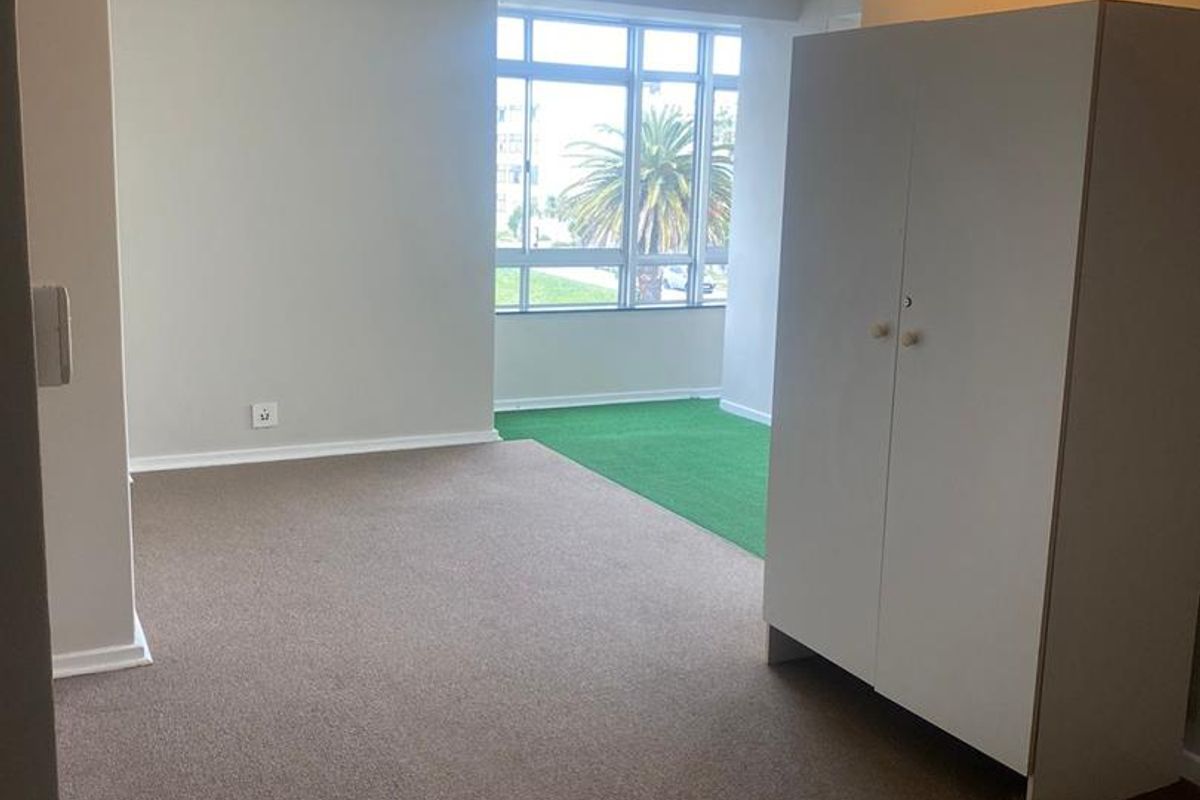 A spacious, carpeted living area featuring a large window that allows for natural light, providing a neutral canvas for interior design.
