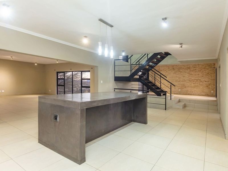 Spacious open-plan living area featuring a modern concrete kitchen island, a striking metal staircase, and a textured stone feature wall with neutral tiled flooring.