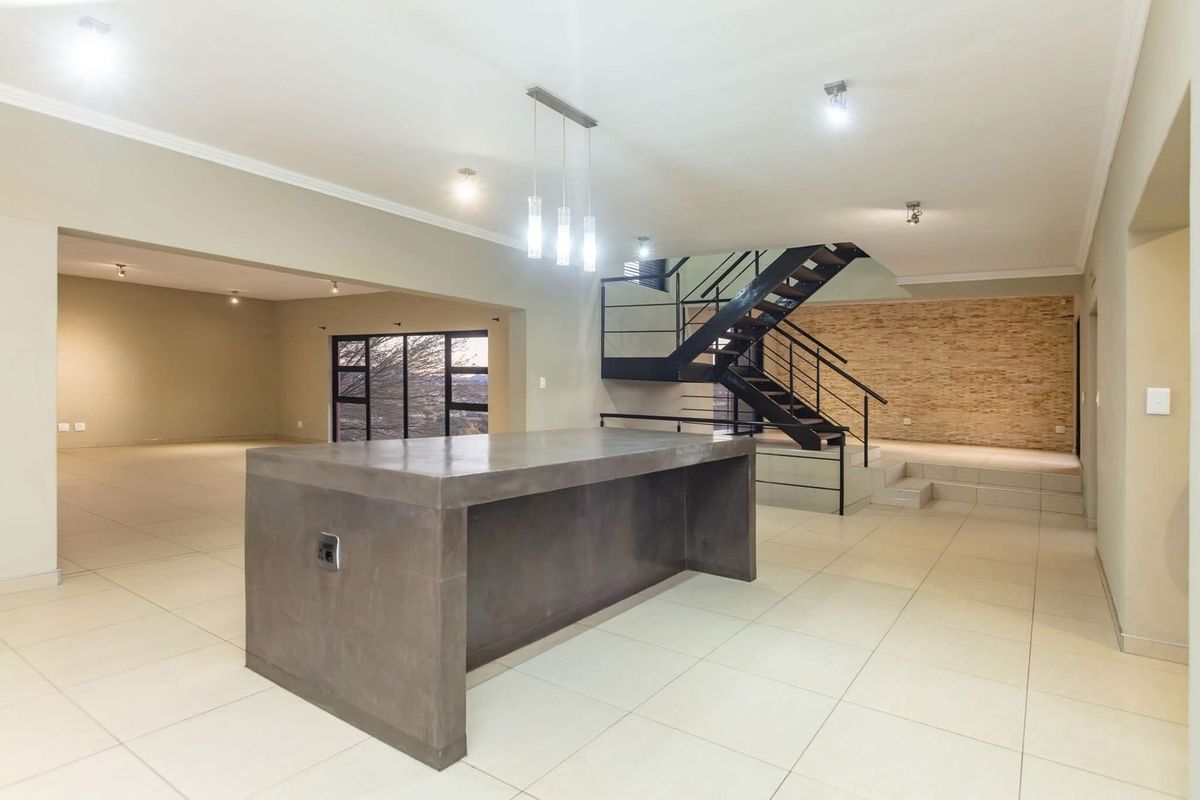 Spacious open-plan living area featuring a modern concrete kitchen island, a striking metal staircase, and a textured stone feature wall with neutral tiled flooring.