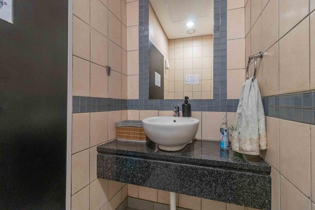 A compact commercial restroom featuring a granite vanity top, vessel sink, and tiled walls with a decorative border.