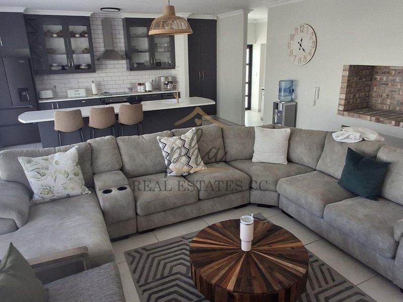 Spacious open-plan living area featuring a modern kitchen with island seating and a cozy brick fireplace, creating a functional and inviting home layout.