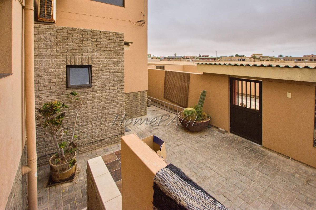 A paved rear courtyard area featuring brick-clad wall accents, a secure metal gate, and exterior drainage downpipes.