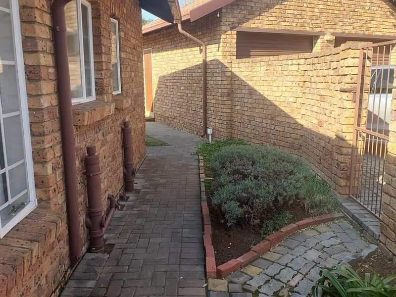 A side view of the townhouse exterior featuring face brick walls, a paved walkway, and a metal gate leading to the property entrance.