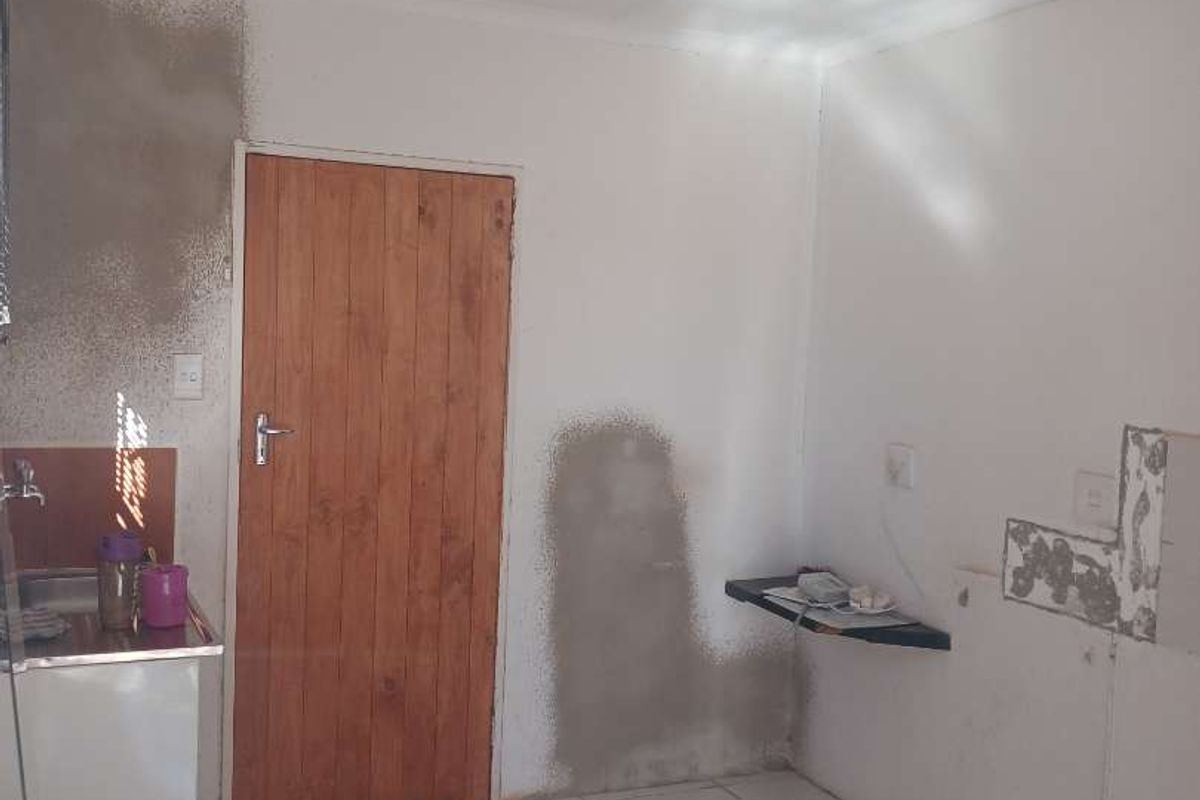 A small utility or kitchen area featuring tiled flooring, a wooden door, and unfinished wall surfaces requiring repair and finishing.