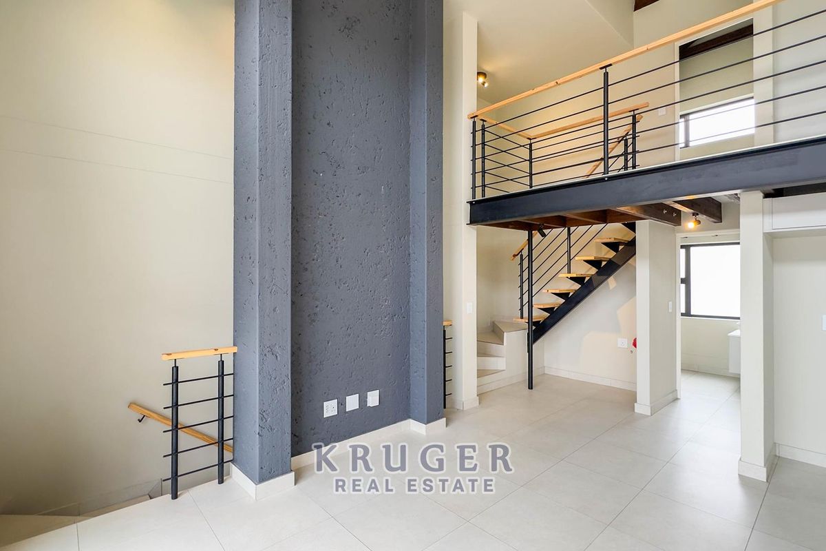 Spacious open-plan living area featuring a double-volume ceiling, a striking dark feature wall, and a modern mezzanine level with a steel staircase.
