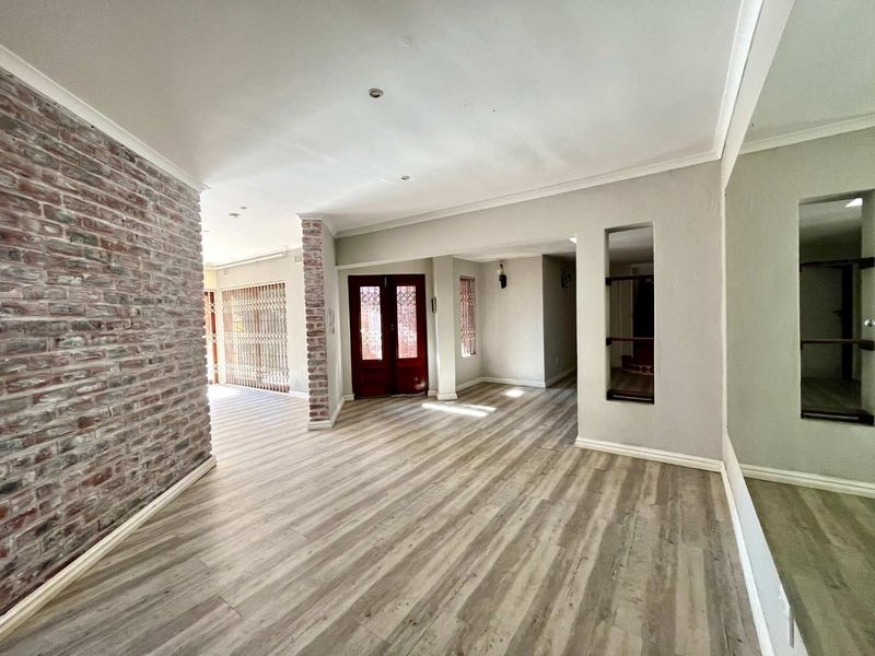Spacious open-plan living area featuring modern laminate flooring, an exposed brick feature wall, and neutral tones, providing a versatile blank canvas for interior design.