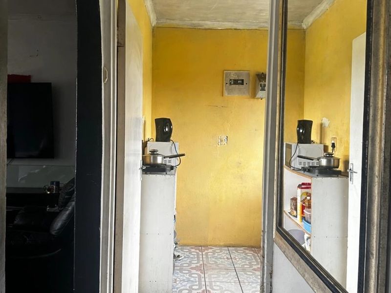 A compact kitchen area featuring patterned floor tiles and yellow wall finishes, accessible through a doorway from the adjacent living space.