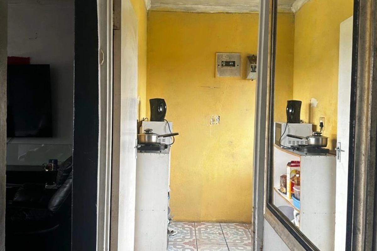 A compact kitchen area featuring patterned floor tiles and yellow wall finishes, accessible through a doorway from the adjacent living space.