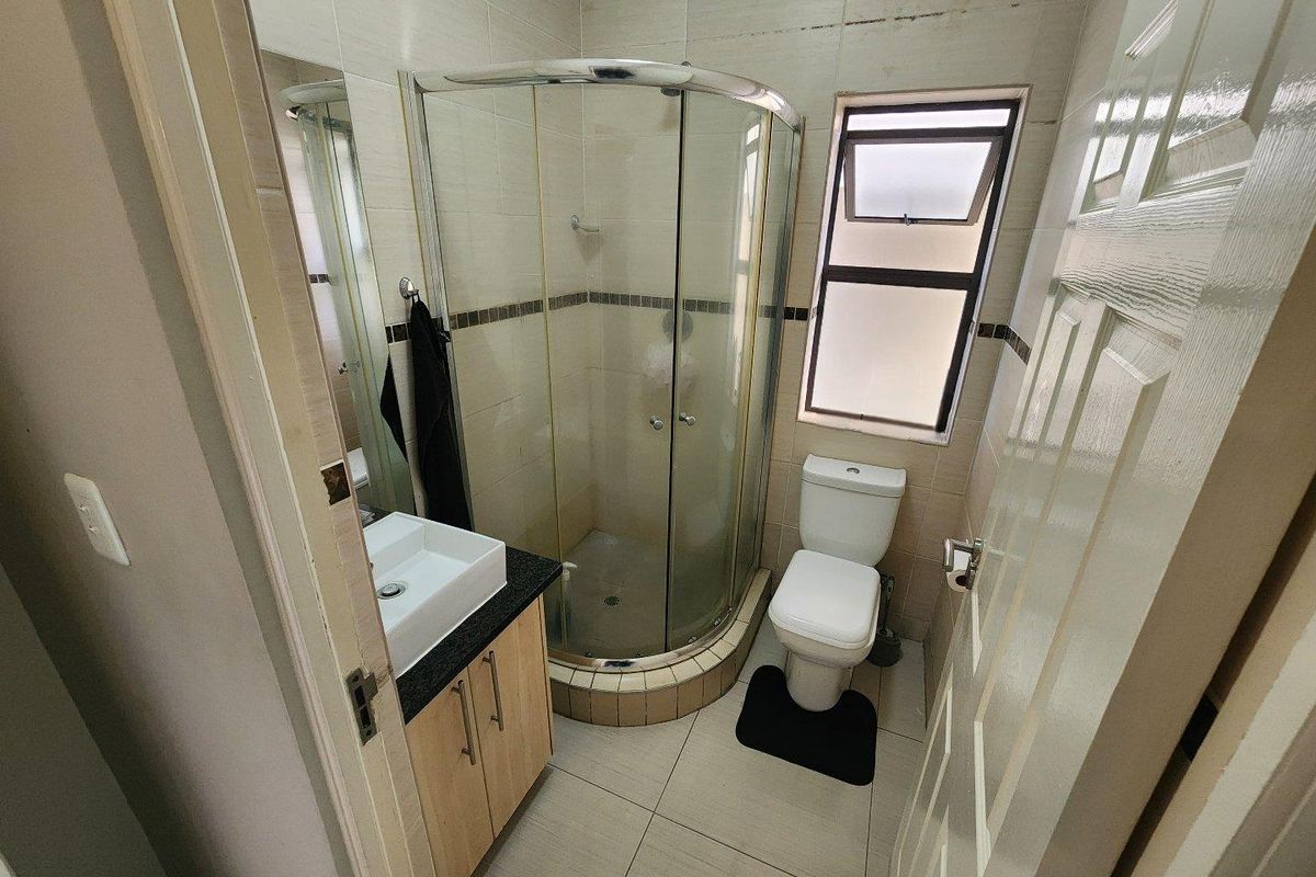 Compact bathroom featuring a corner glass shower enclosure, a modern vessel sink with vanity cabinet, and a standard toilet.