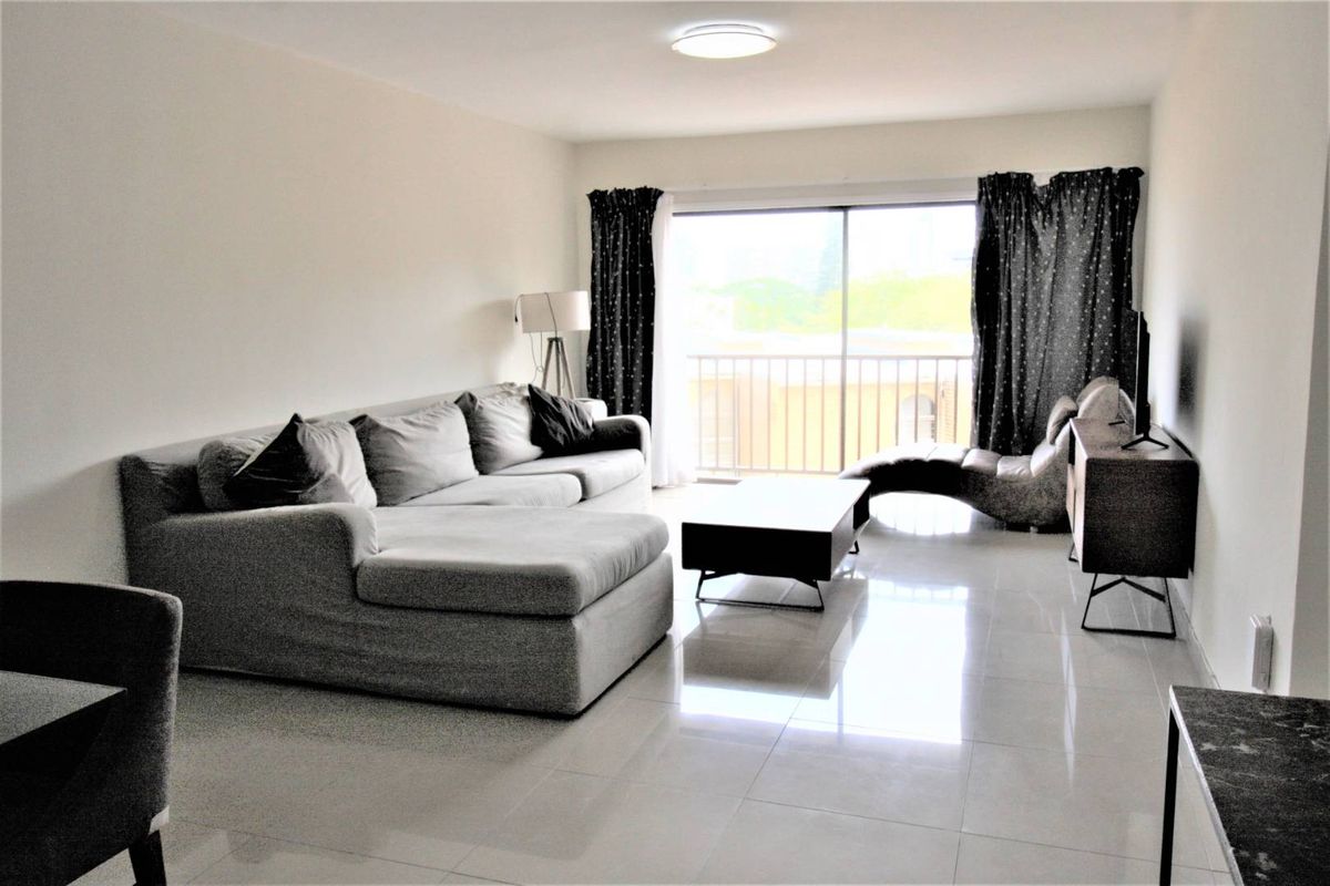 Spacious living room featuring large sliding glass doors that open onto a private balcony, finished with neutral tiled flooring throughout.