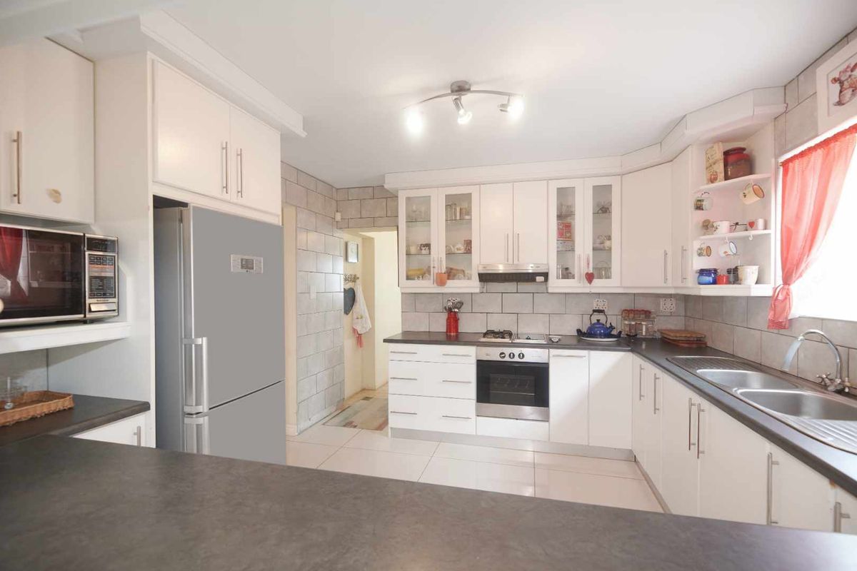 A functional kitchen featuring white cabinetry, dark countertops, a built-in oven, gas hob, extractor fan, and a double stainless steel sink.
