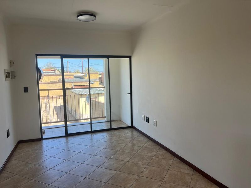 An empty living room featuring tiled flooring and a large sliding glass door providing access to a balcony.