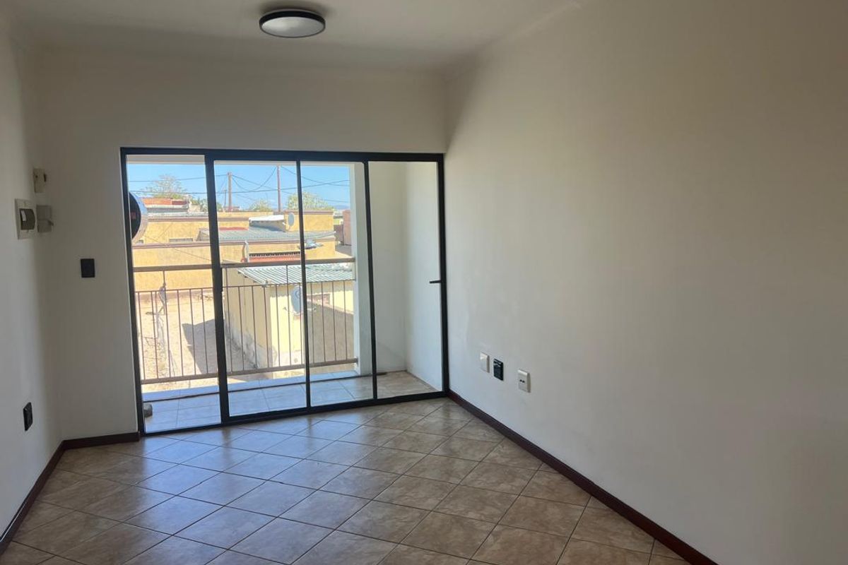 An empty living room featuring tiled flooring and a large sliding glass door providing access to a balcony.