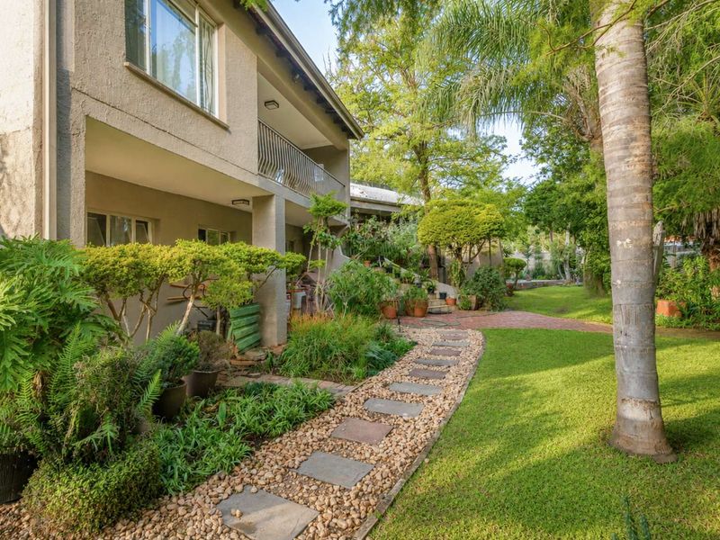 A well-maintained rear garden featuring a stone pathway, lush landscaping, and a covered balcony with metal railings overlooking the yard.