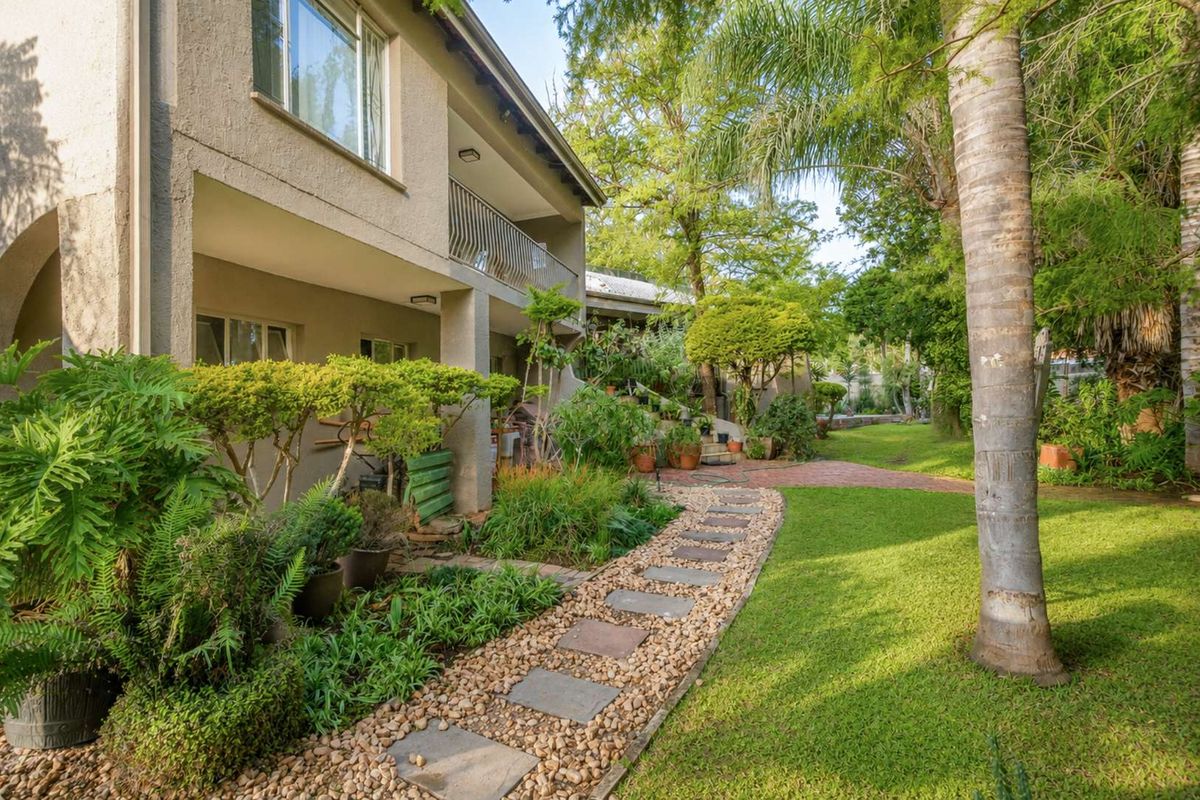 A well-maintained rear garden featuring a stone pathway, lush landscaping, and a covered balcony with metal railings overlooking the yard.