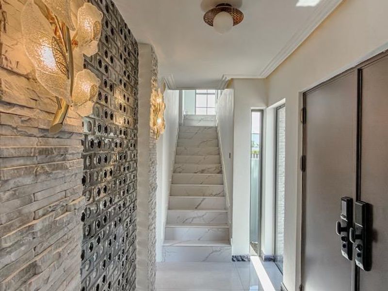 Modern entrance foyer featuring a striking combination of stone cladding and glass block walls, leading to a marble-tiled staircase with contemporary lighting.