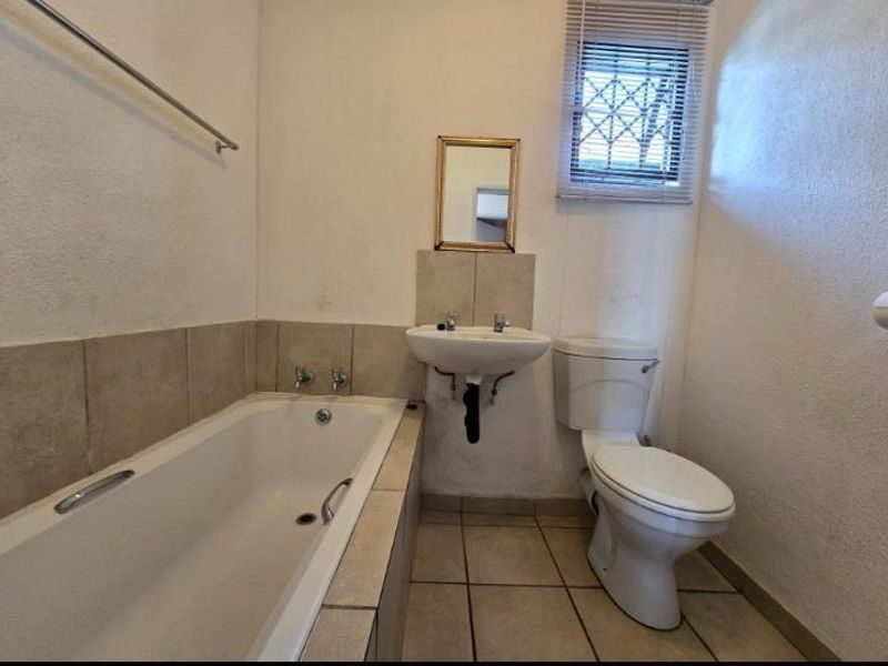 A functional bathroom featuring a built-in bathtub, wall-mounted basin, and toilet with tiled splashbacks and flooring.