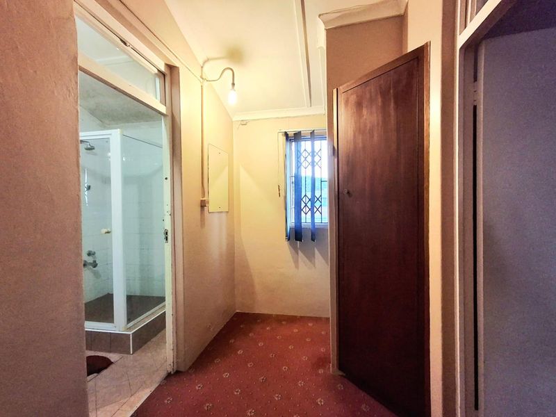 A functional hallway area featuring carpeted flooring, a built-in cupboard, and direct access to an adjacent shower room.