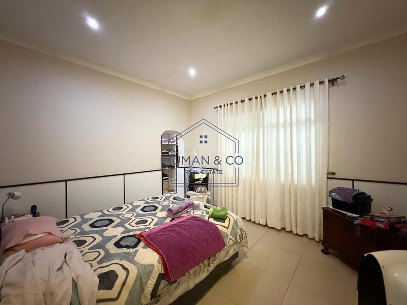 A bedroom featuring tiled flooring, recessed downlighting, and built-in wall paneling, with a window dressed in curtains.